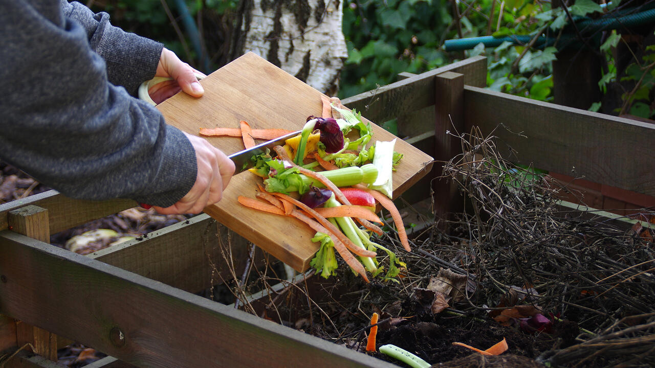 Person scraping compost vegetables in a compost pile.