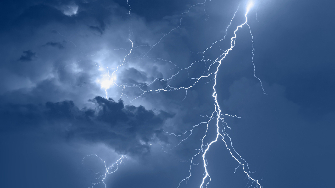 Lightning stirkes light up a cloudy, blue night sky.