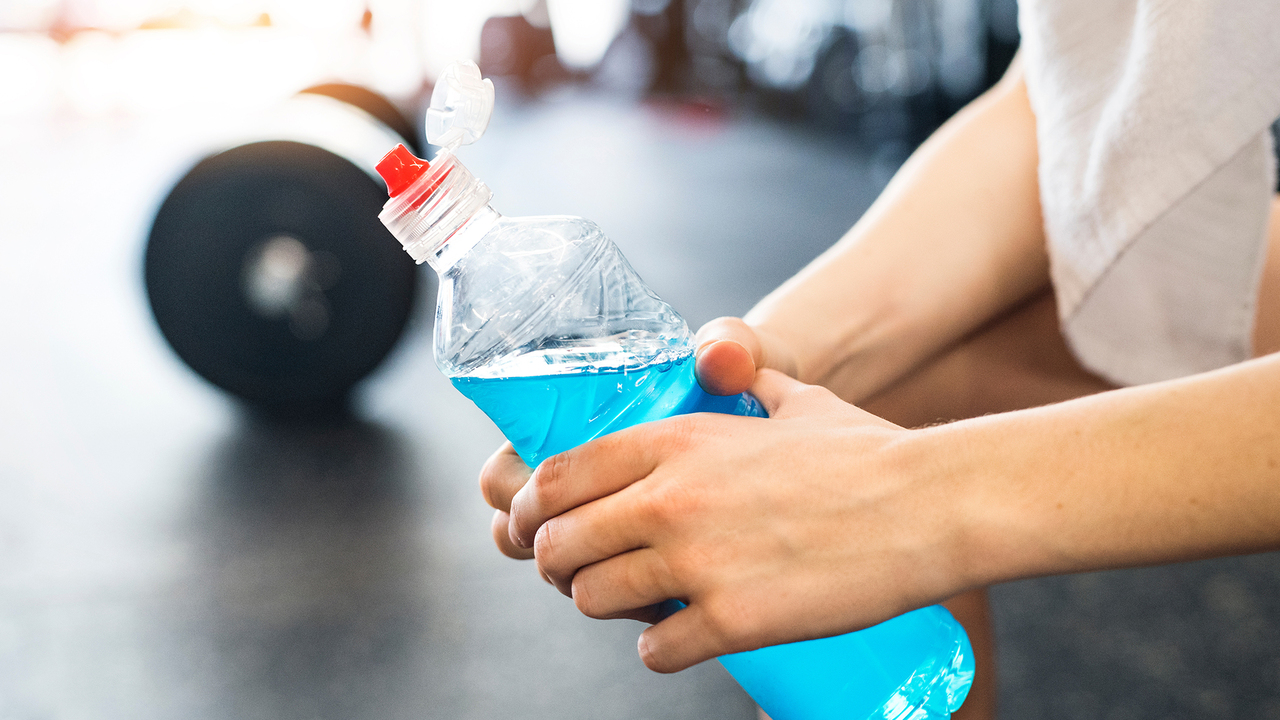 Closeup of hands holding a blue sports drink after a hard workout in the gym. 