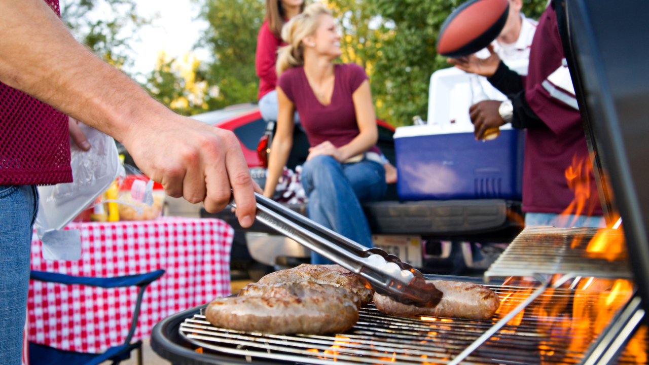 A person grills sausages at a tailgate.