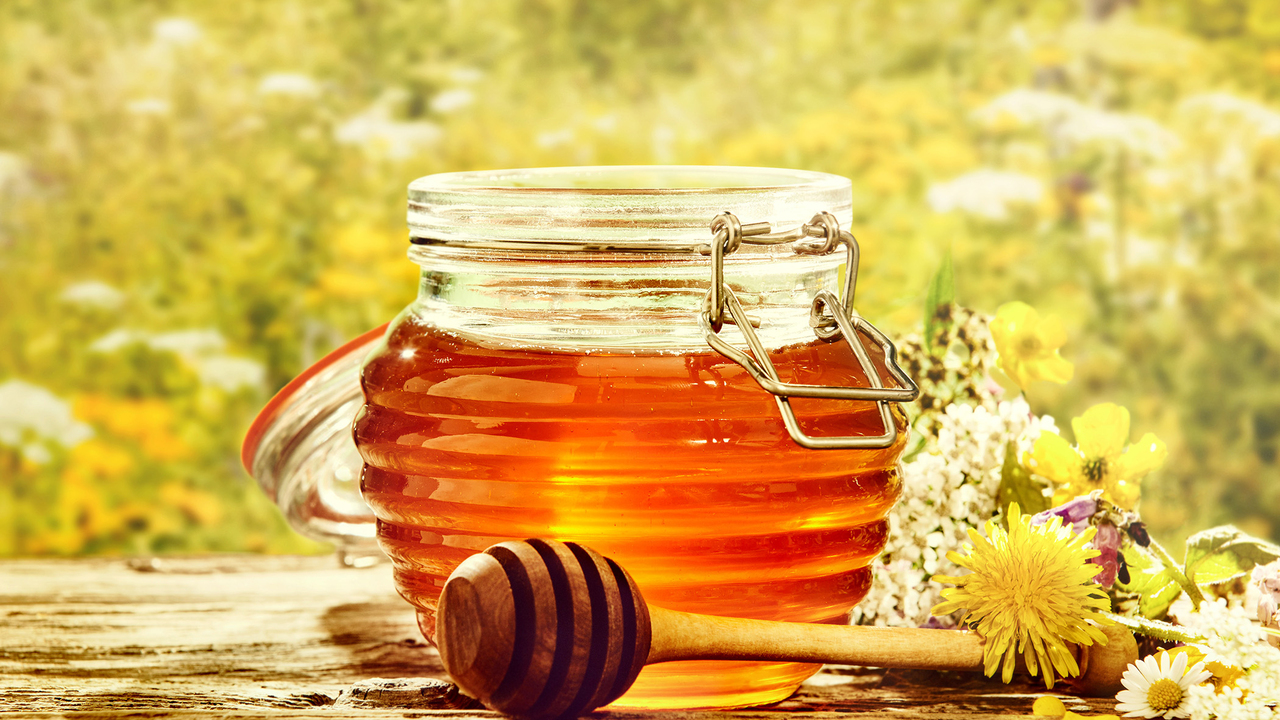 Bowl of honey with dipper in a field of flowers