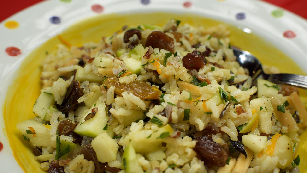 A mixture of rice, apples, raisins and almonds is displayed in a colorful bowl.