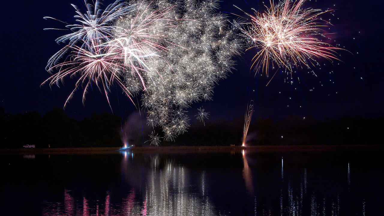Fireworks explode against a dark sky and above a large body of water.