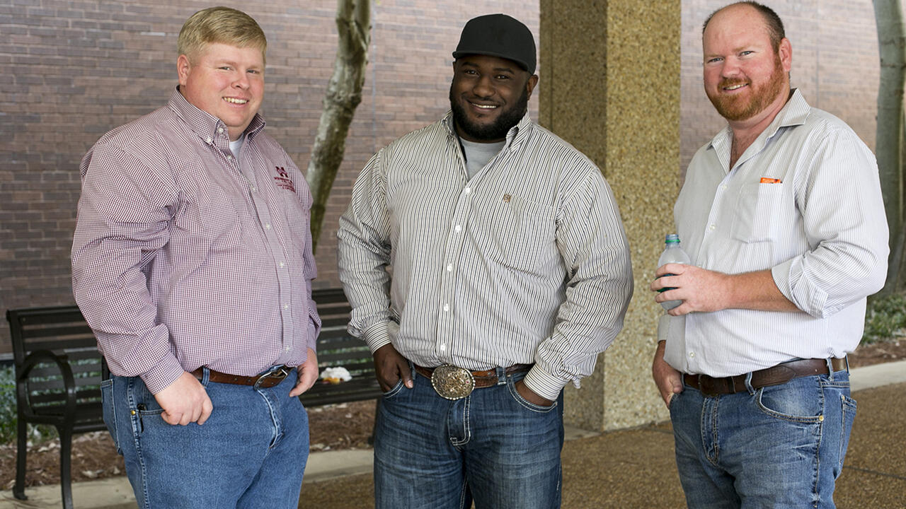 Three adult males stand outside a building.
