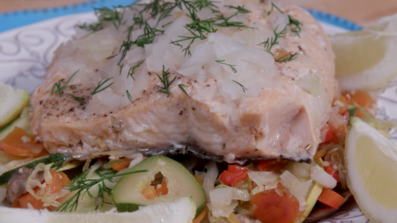 A steamed salmon filet sprinkled with onions and dill sits atop roasted vegetables.