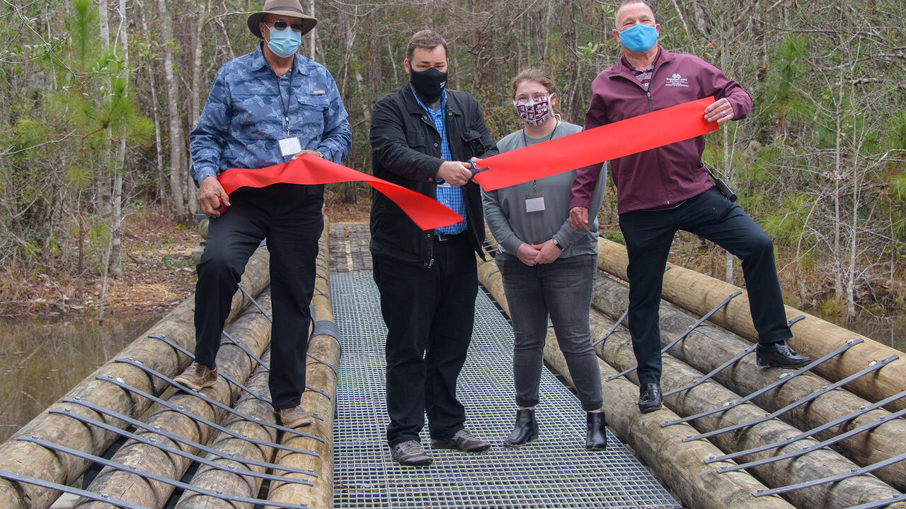 Four people stand on a bridge while cutting a ceremonial ribbon.
