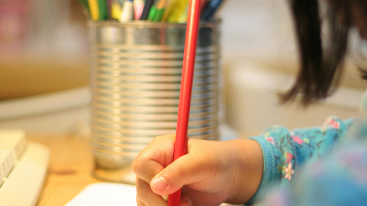 A child uses a colored pencil to write on a sheet of paper.