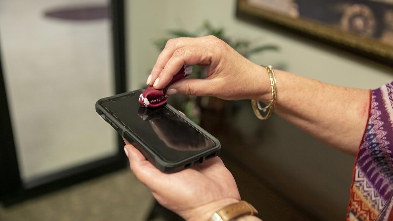 One hand holds a phone while the other hand wipes the screen with a small cloth.