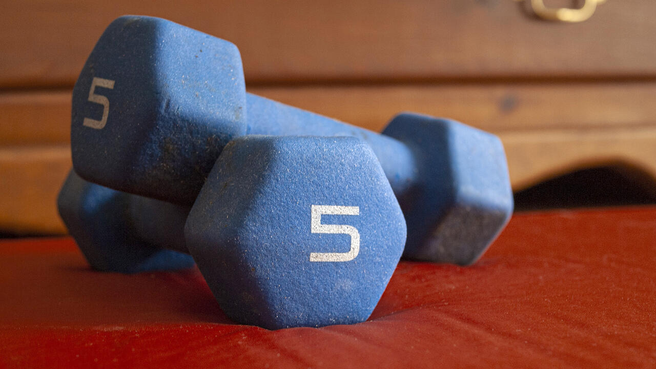 Two blue dumbbells are stacked on a bedroom floor.