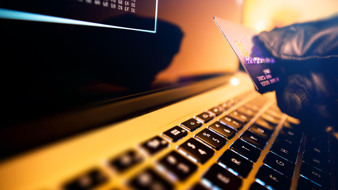 A gloved hand holds a credit card above a keyboard.