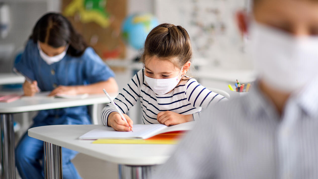 Three students wear face masks as they sit at their desks.