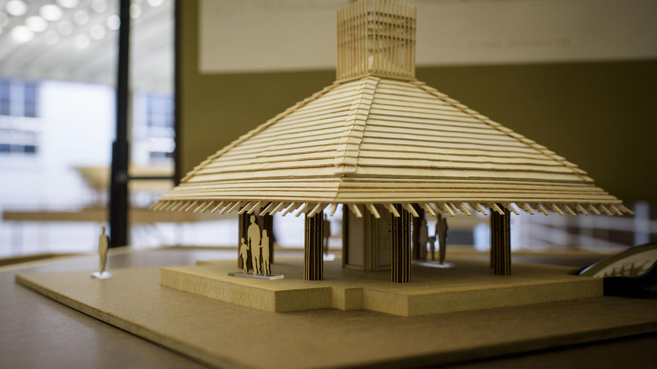 A wooden model of a building rests on a table in an exhibit hall.