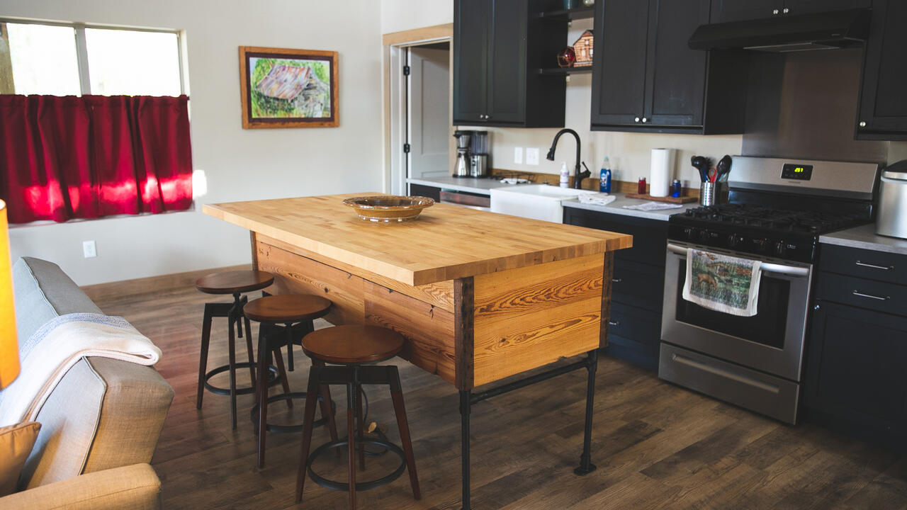 A serving island and three stools sit in a kitchen.