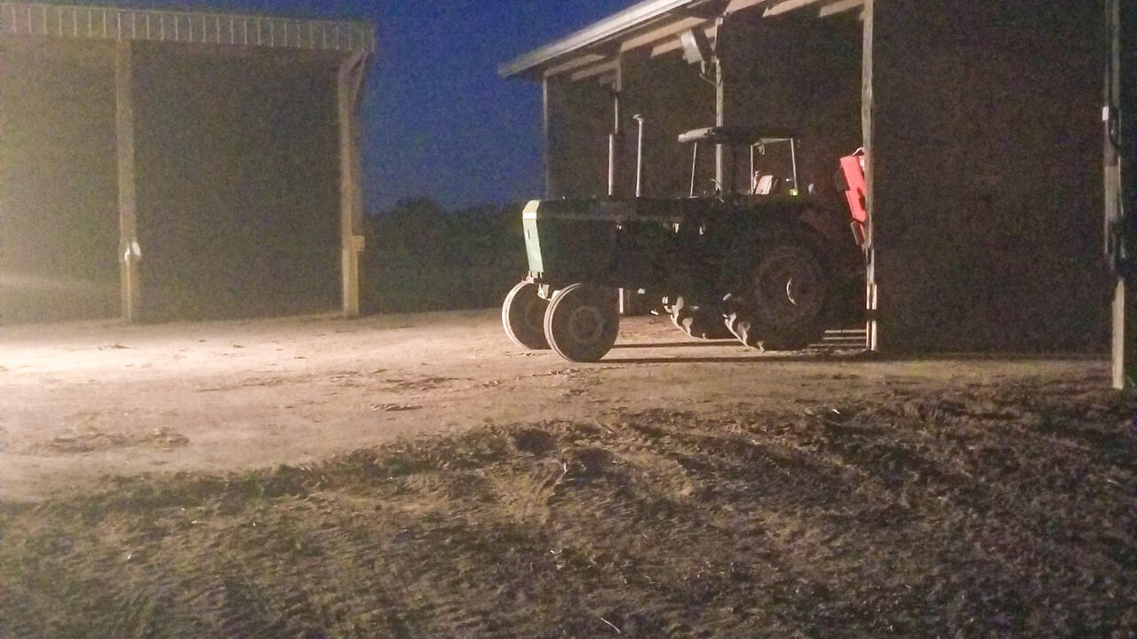 A tractor parked outside of a shed at night.