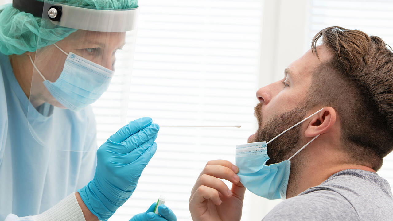 Medical worker in protective clothing takes a throat swab from a male patient.