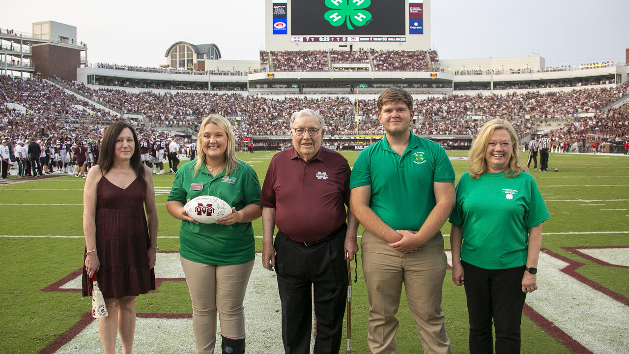 Five people pose for a photo on a football field.