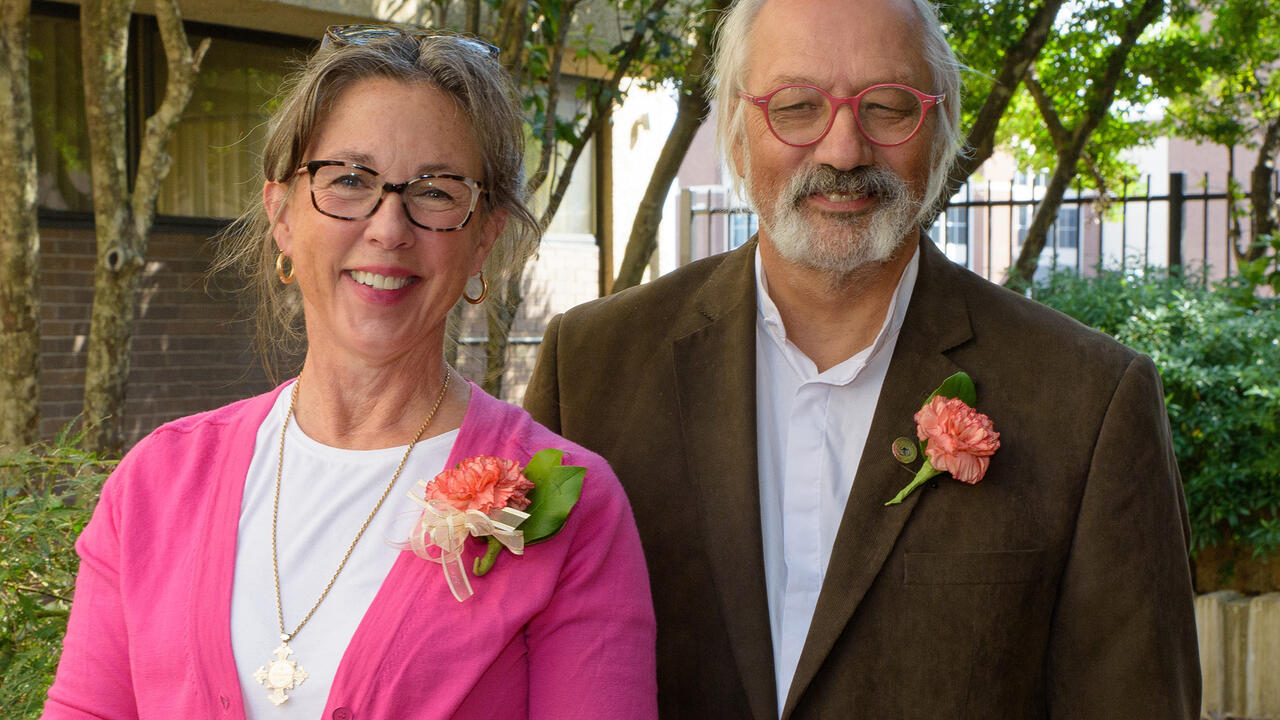 A man and a woman pose in a garden.