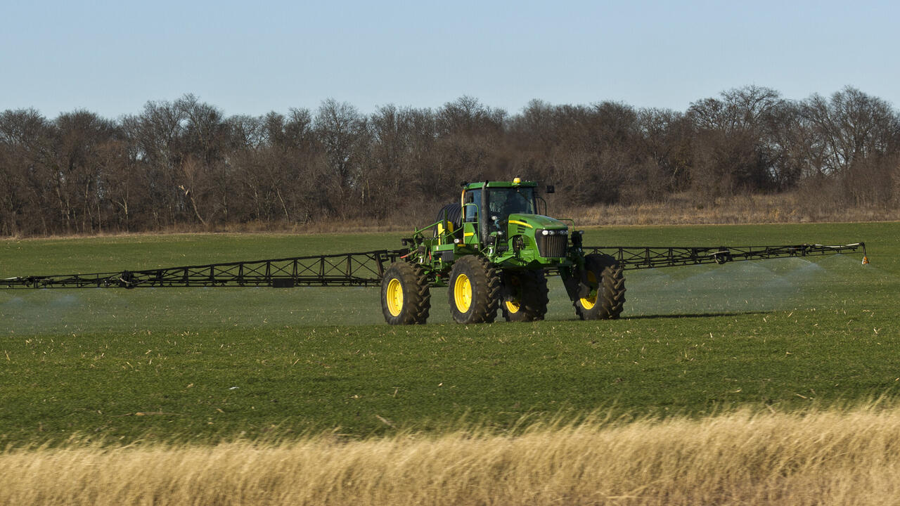 A tractor with a spray rig crosses a wheat field.