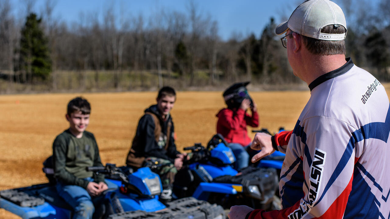 Three young people sit on ATVs as they listen to their instructor.