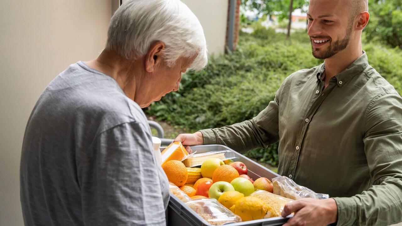 A man delivers a food box to a senior citizen.