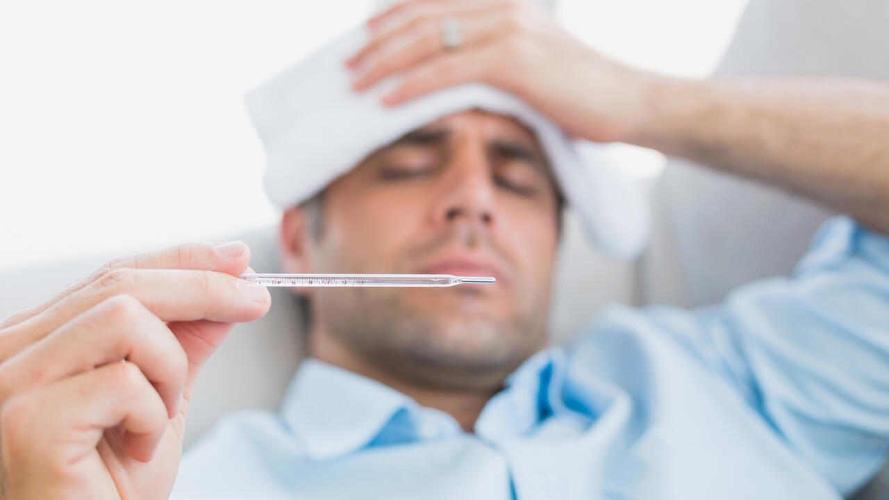 Sick man lying on sofa checking his temperature at home in the living room