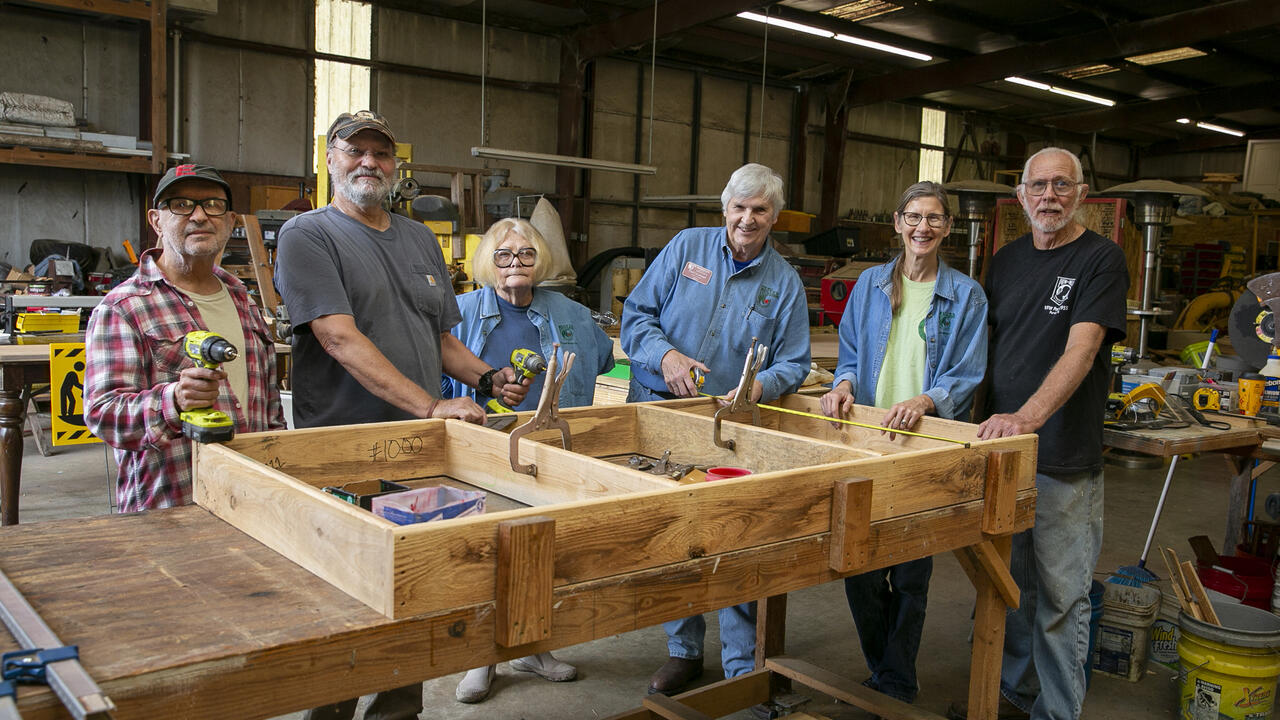 A group of people stand in a shop around a woodwork project.