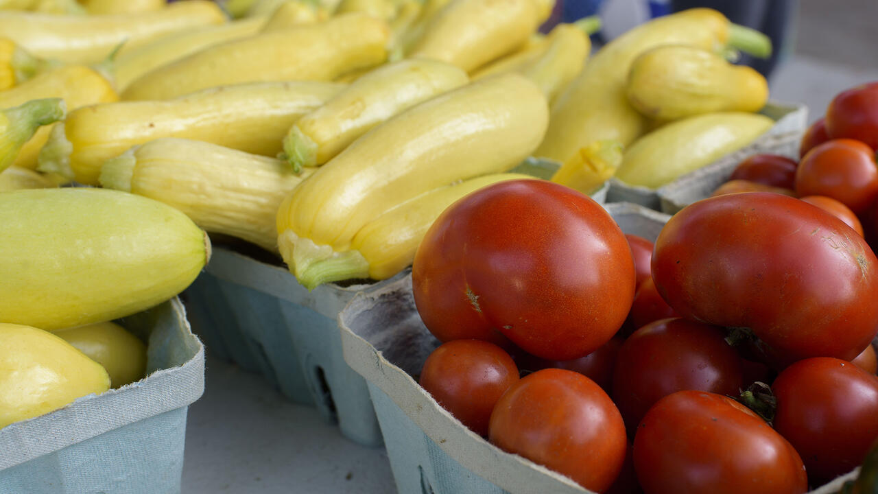 Close up of tomatoes and yellow squash in farmers market baskets.