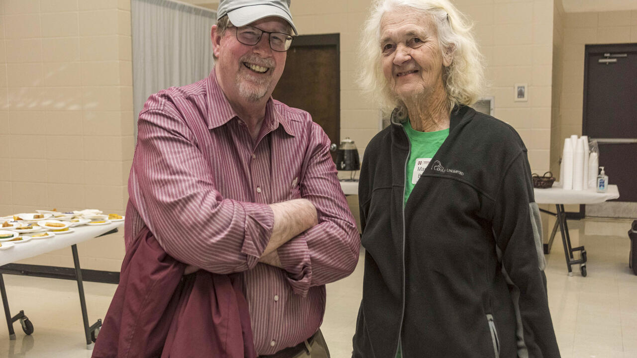 A man and a woman stand together in a meeting space.