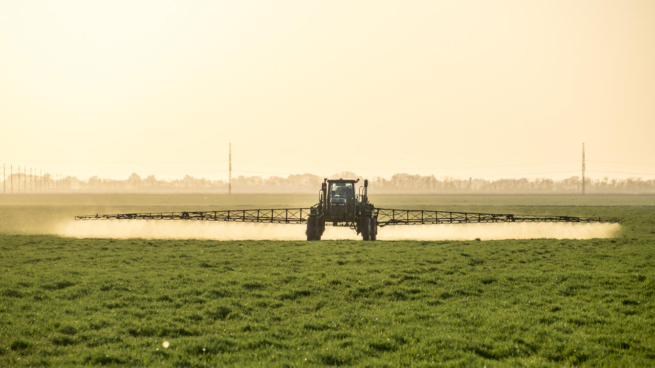 A tractor with a boom arm sprays crops.