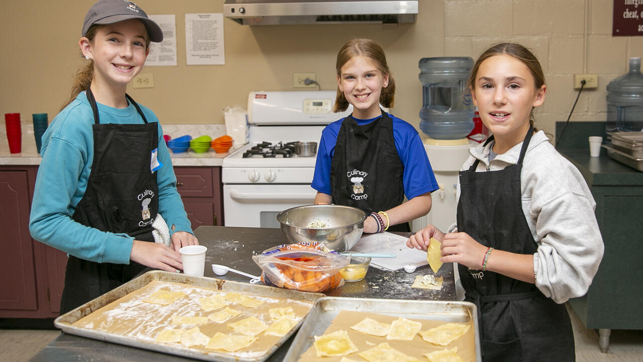 Three girls work with dough sheets at a table.
