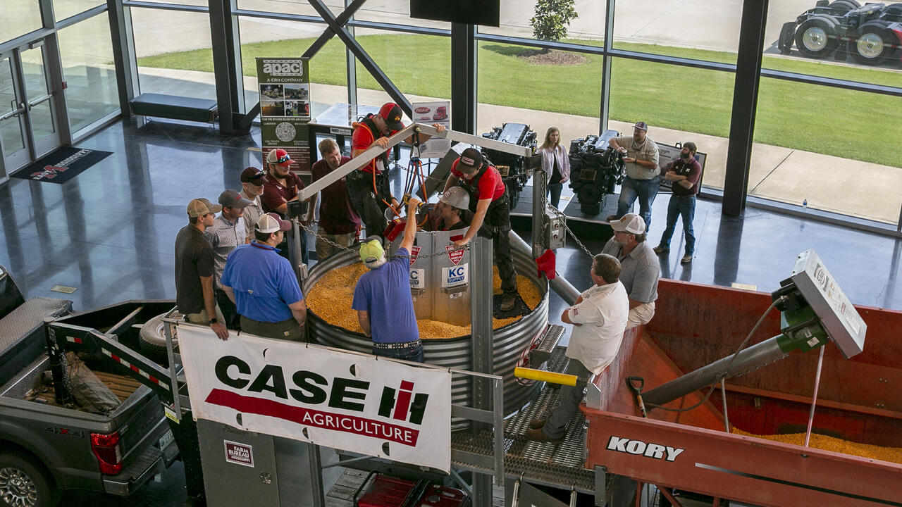 Overhead shot of a dozen people peering into a grain bin with one person inside.