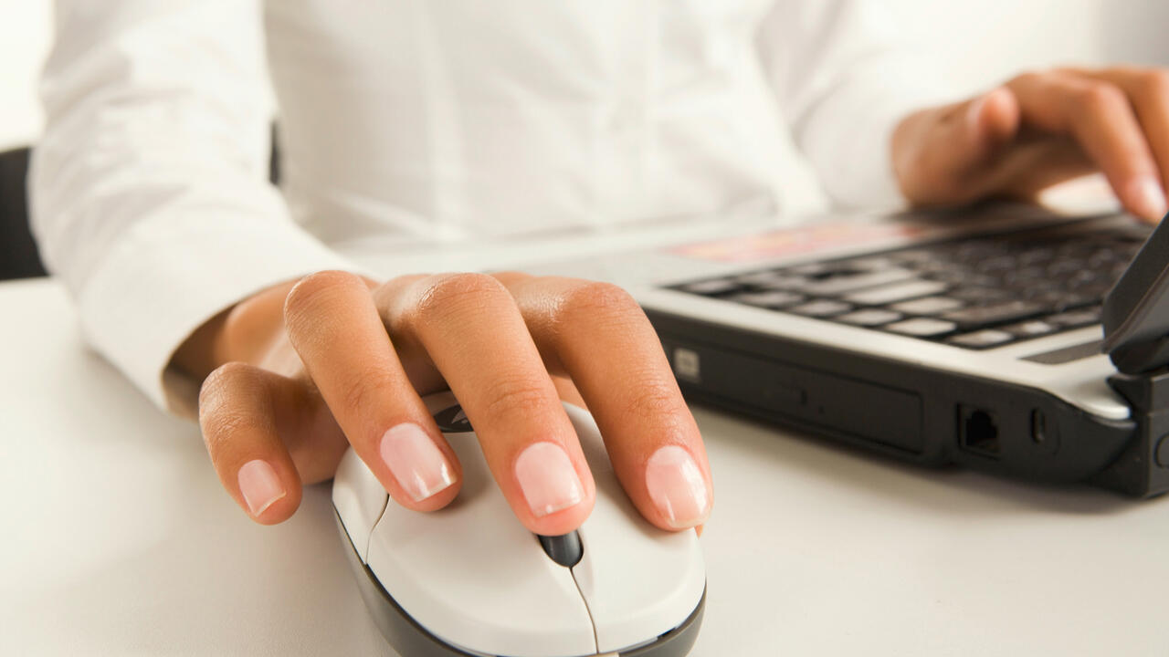 A person’s right hand rests on a computer mouse while their left hand rests on a laptop keyboard.