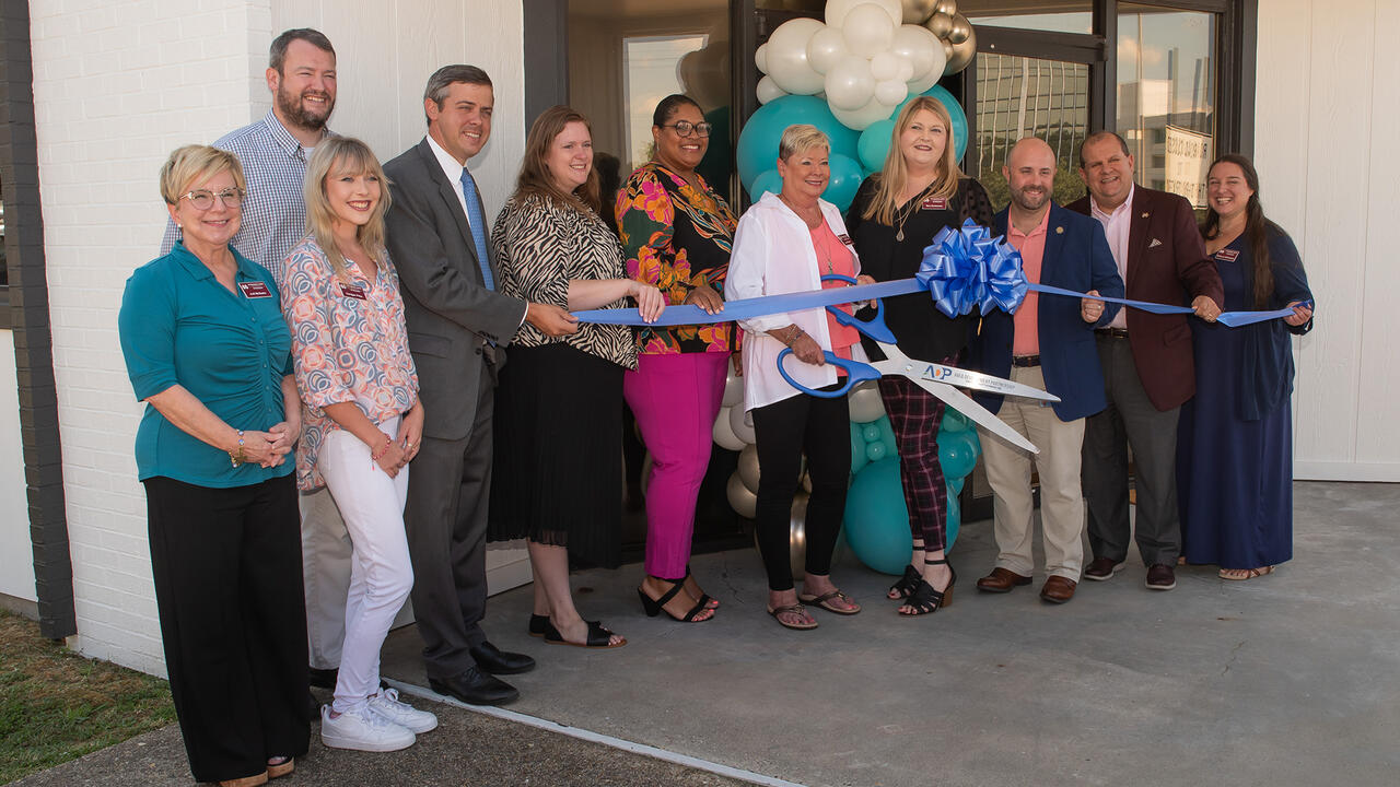 A group of people hold a ribbon in front of a building entrance.