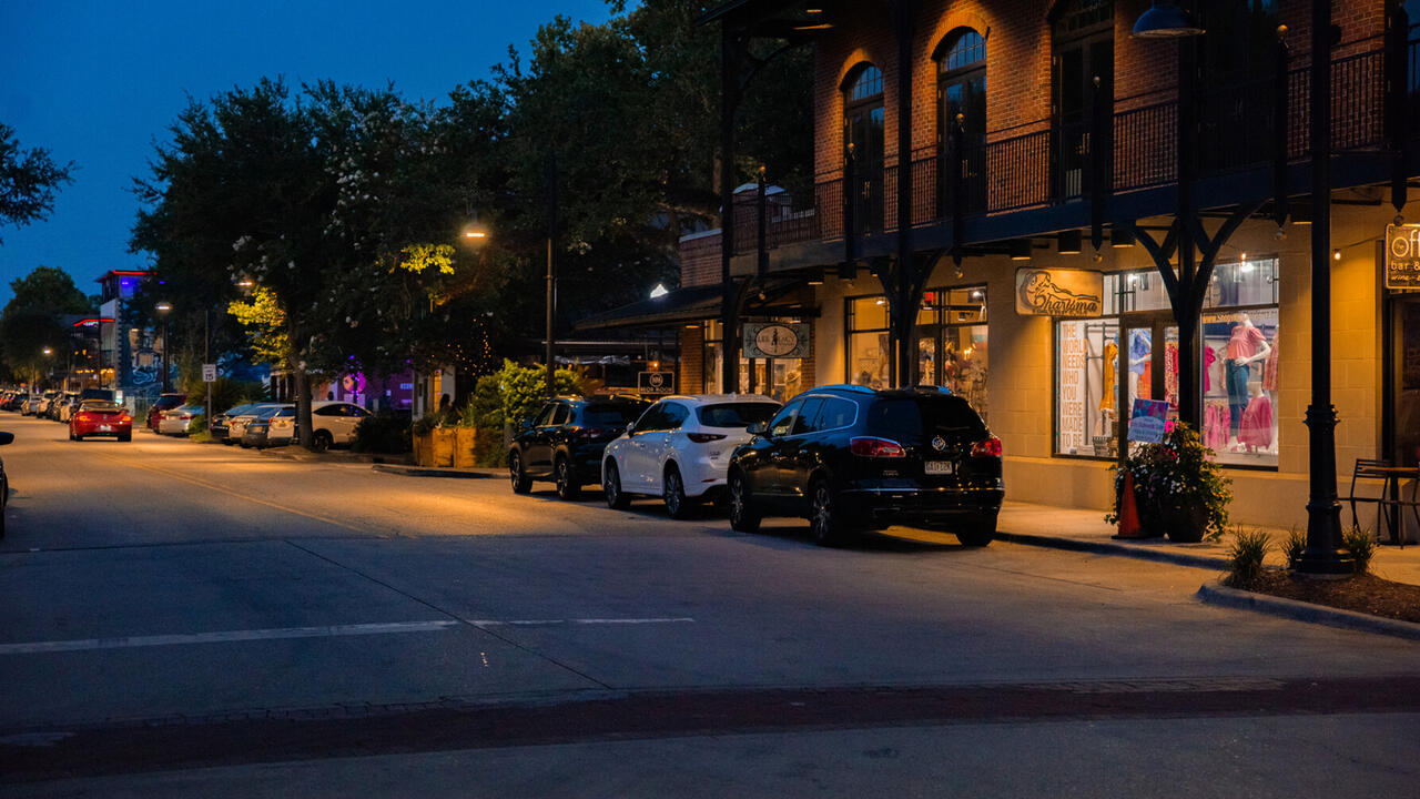 A night view of a downtown street in Ocean Springs, Mississippi, lined with shops and parked cars.