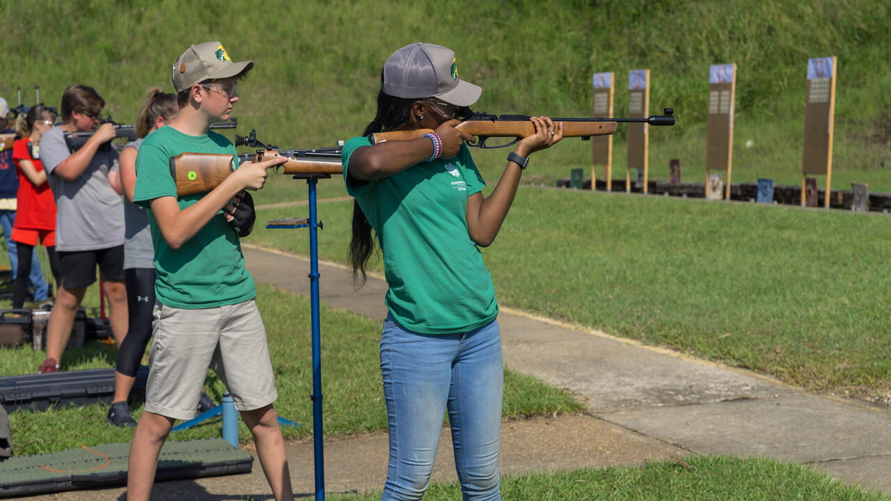 Teenagers at a shooting sports competition aim shotguns at targets.