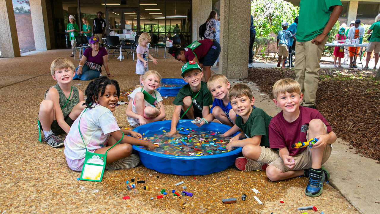 Seven young children playing with legos in a small pool of water.