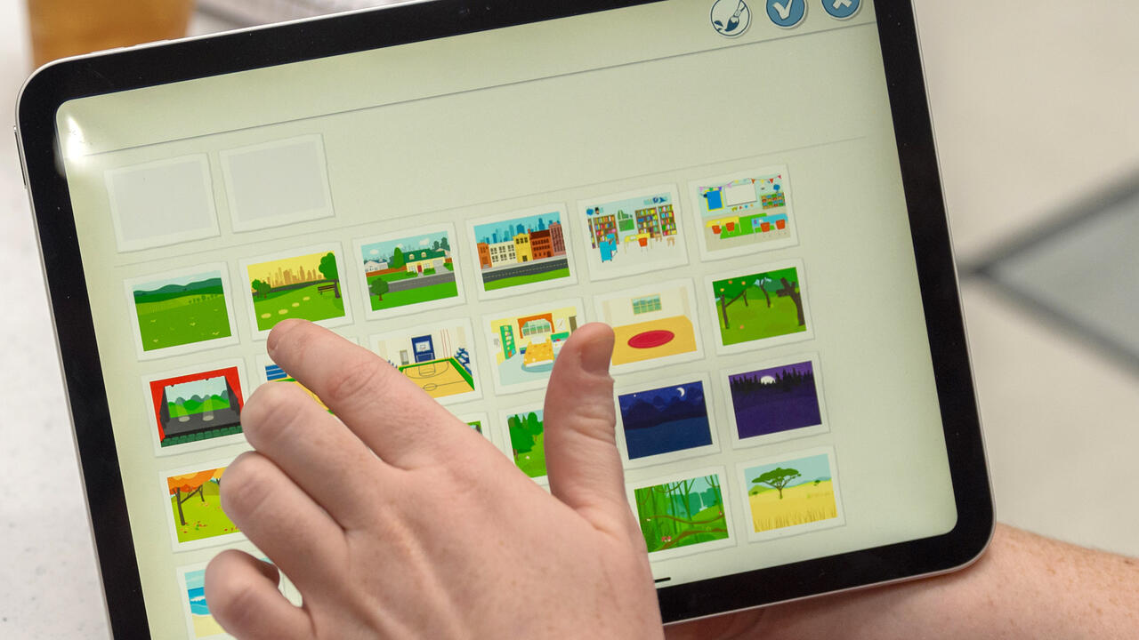 A hand touching the screen of a tablet to pick a picture from a selection.