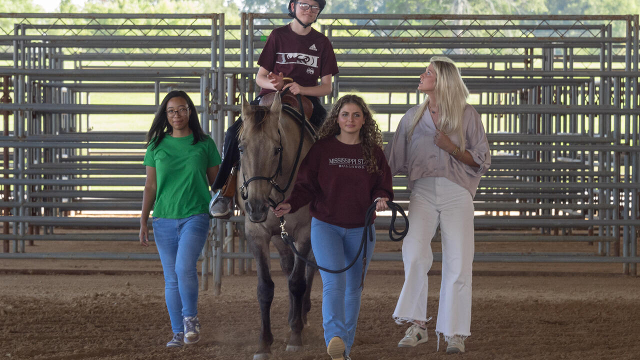 Boy riding a horse surrounded by three people.