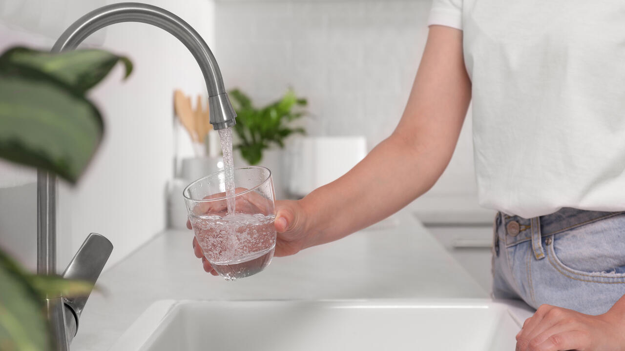 A person fills a glass with water at a kitchen sink.