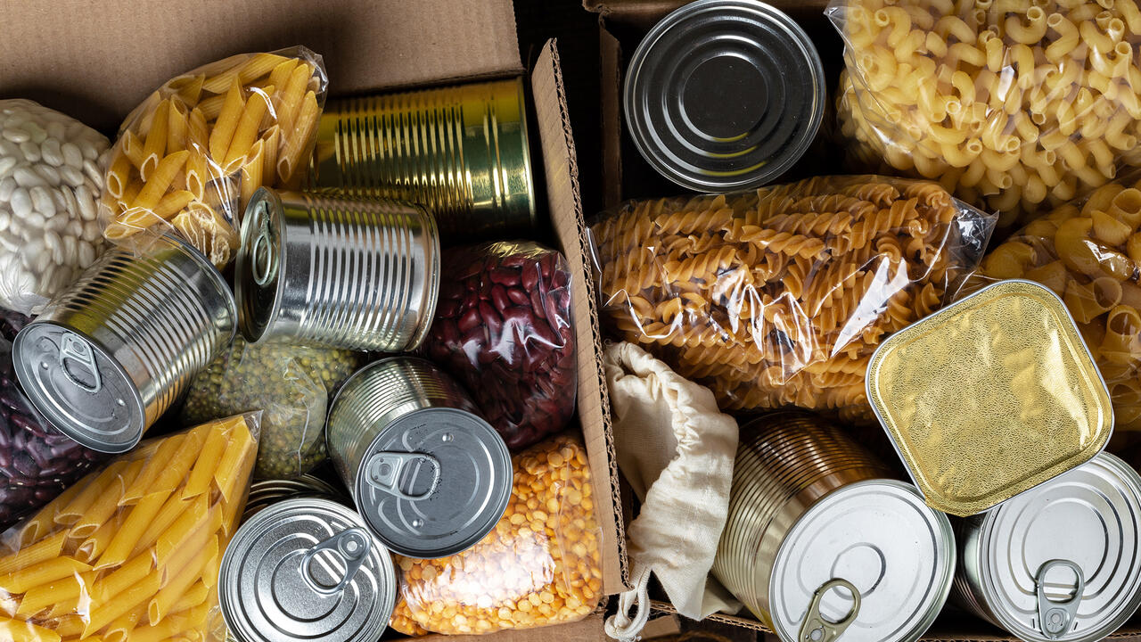 A box of food to donate, including beans, pasta, and canned goods.