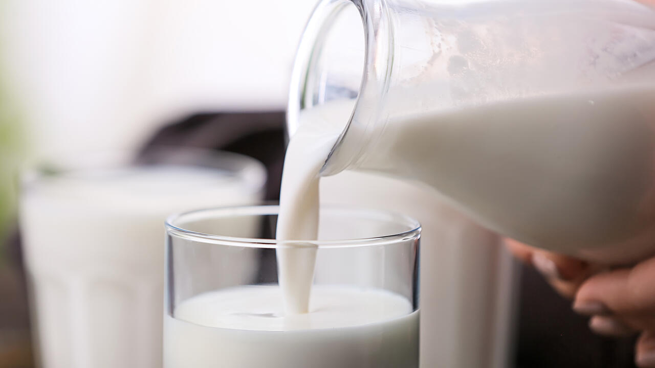 Hand pours milk from a glass bottle into a cup