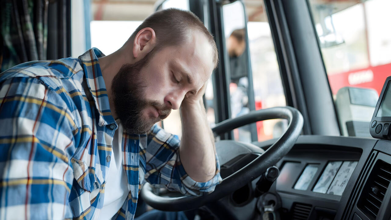 Tired man rests his head in a truck cab.
