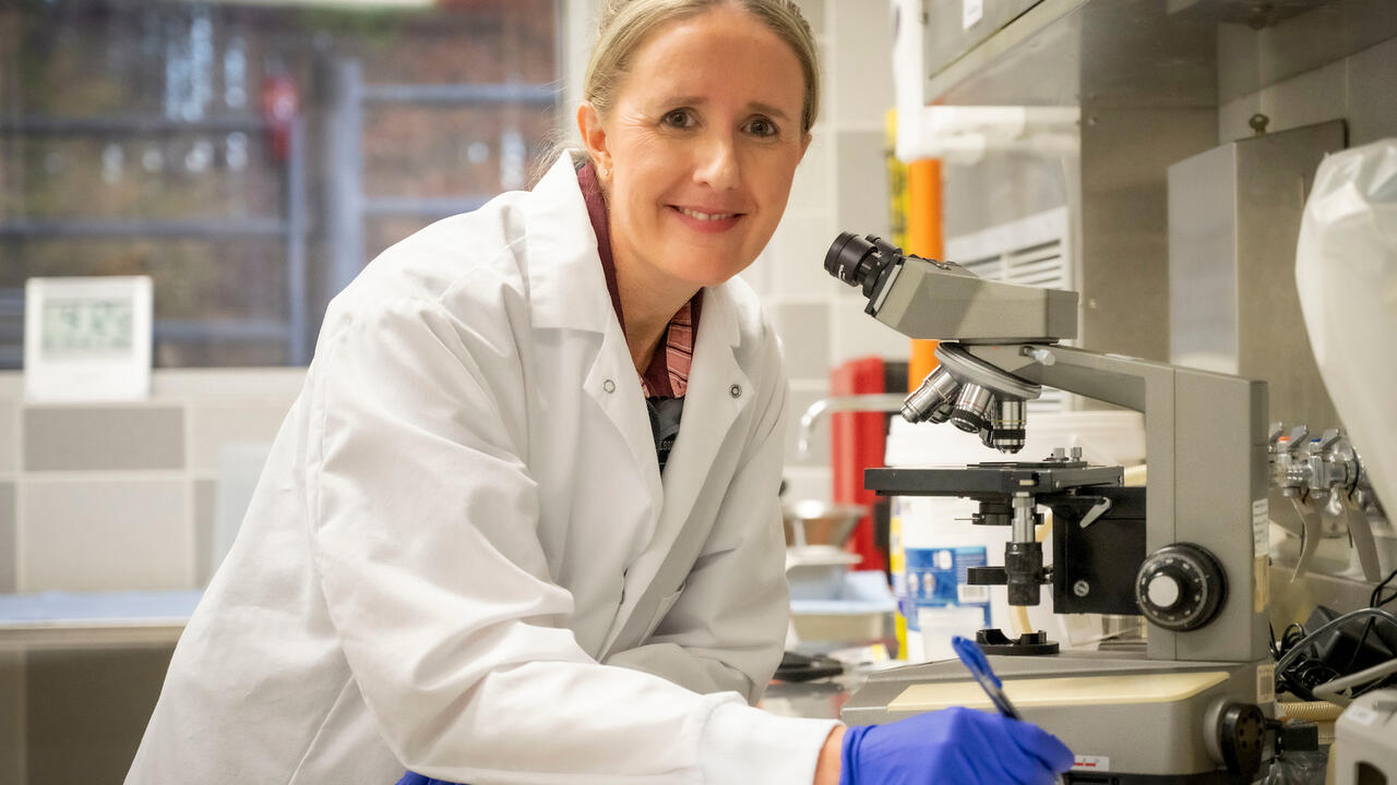 Doctor in a white coat smiling and standing beside a microscope