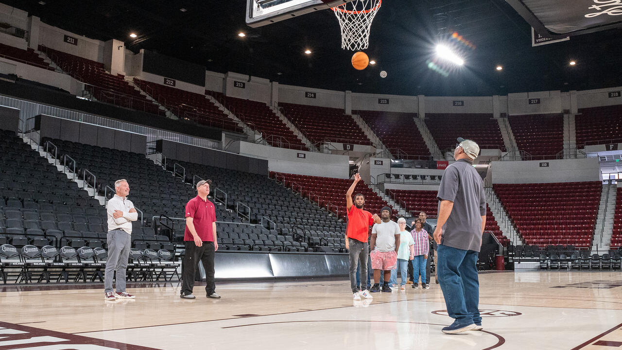 One man shoots a basketball on a court as others stand nearby.