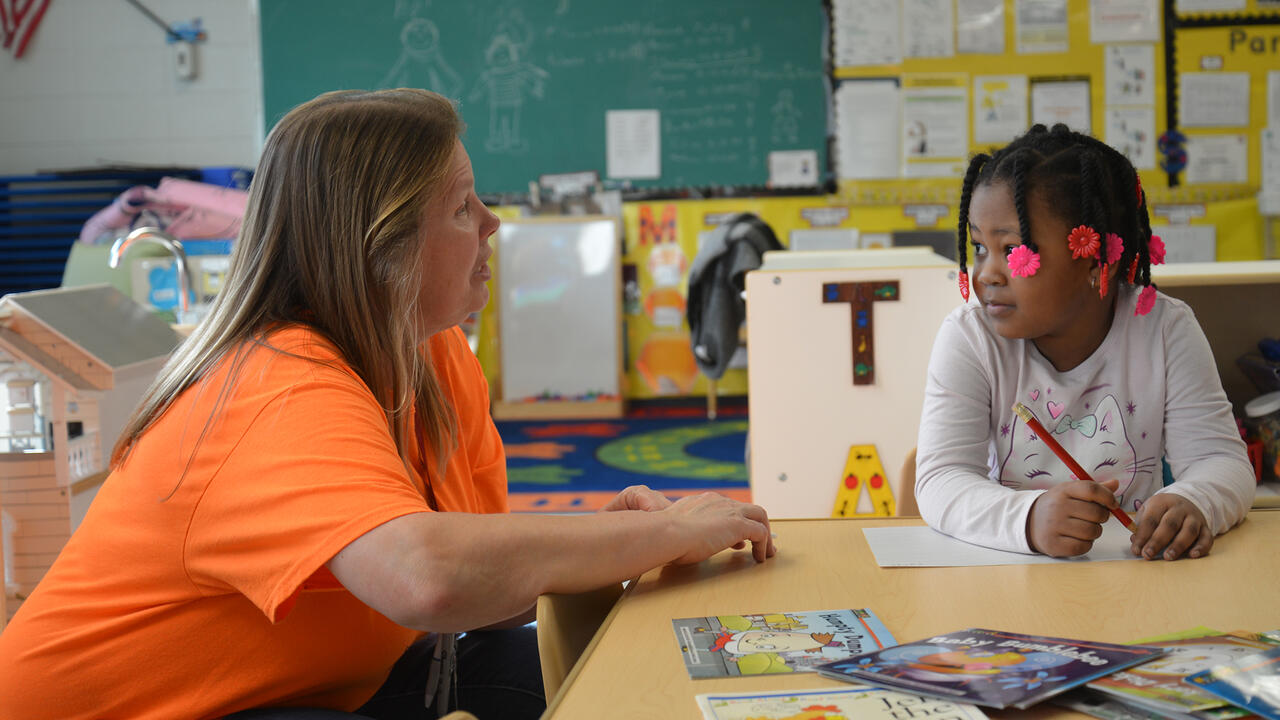 A teacher speaks to a child in a classroom.