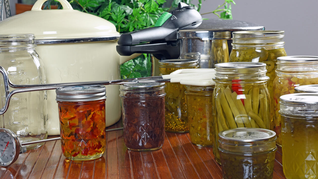 Canning equipment and canned foods sit on a counter.