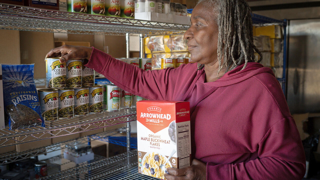A woman puts nonperishable food on pantry shelves.