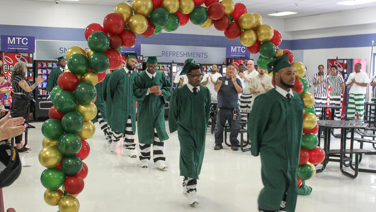Graduates in gowns walk under a balloon arch.