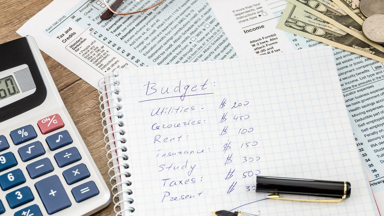 A calculator, handwritten budget, and paperwork sits on a table.