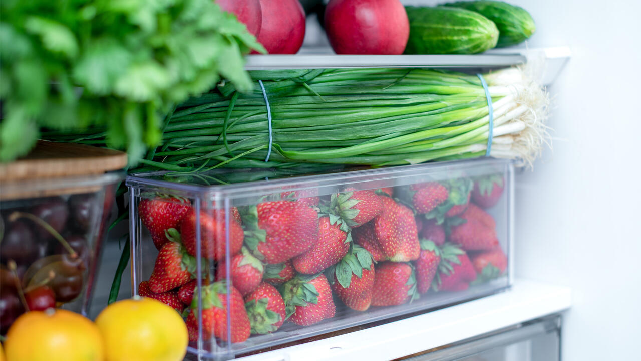 Fruits and vegetables in clear containers in a fridge.